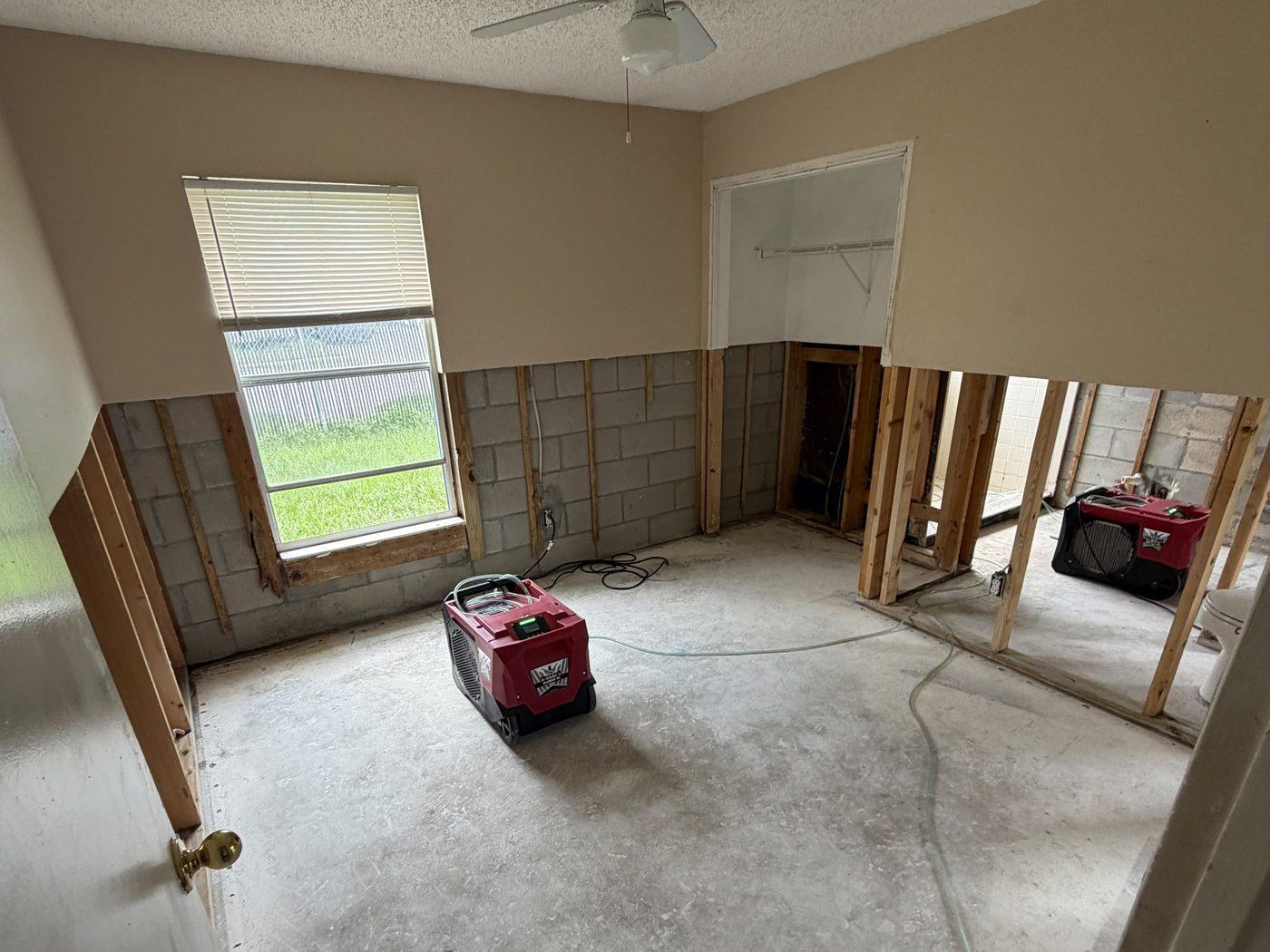 The same bedroom with the carpet removed down to the slab, a flood cut in the drywall and a dehumidifier running