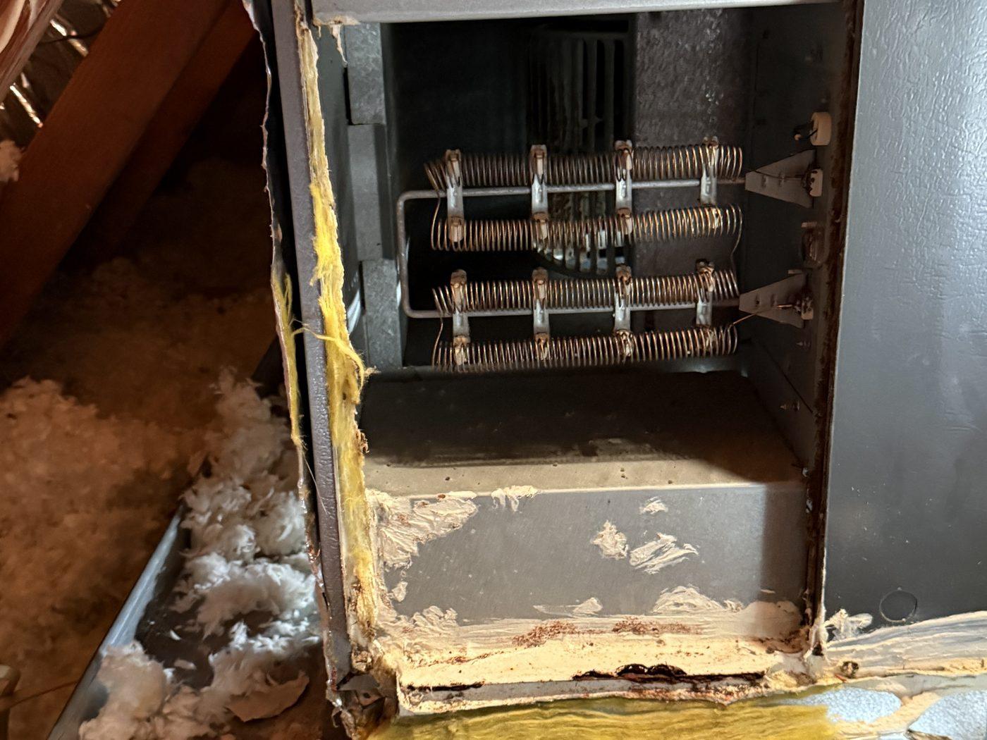 Inside the old air handler, cabinet rusted, perimeter sealant spent and loose insulation around it