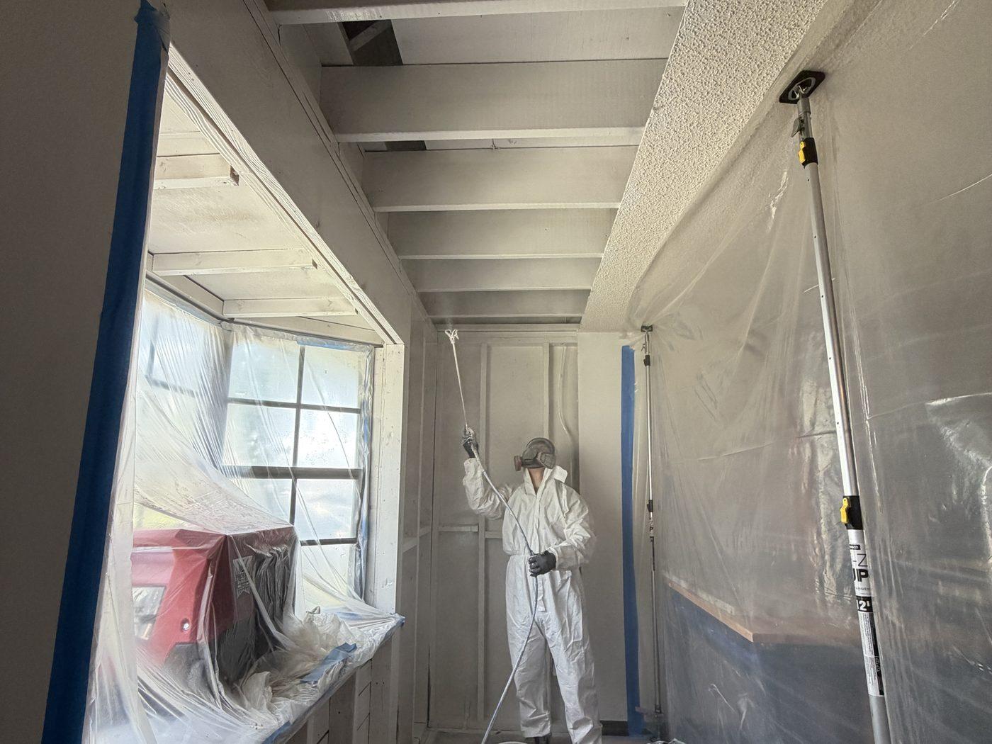 Technician in a protective suit sealing the exposed ceiling framing inside containment after the mold removal