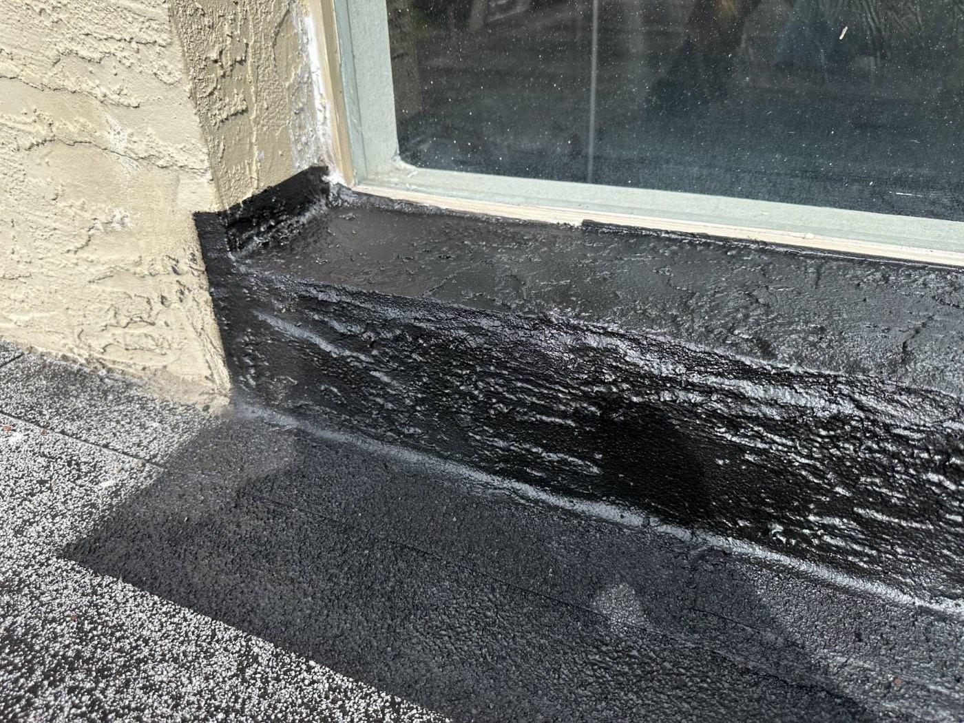 The same window sill sealed with a black waterproofing membrane over the joint and the roof edge